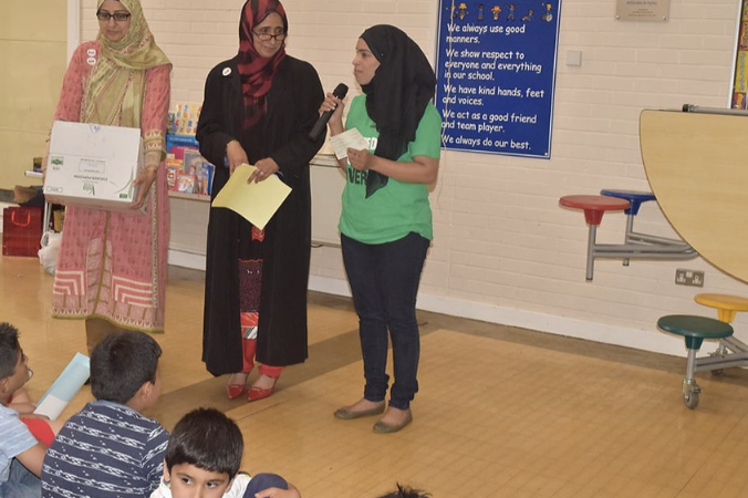 Three women stood up speaking toa group of children indoors.